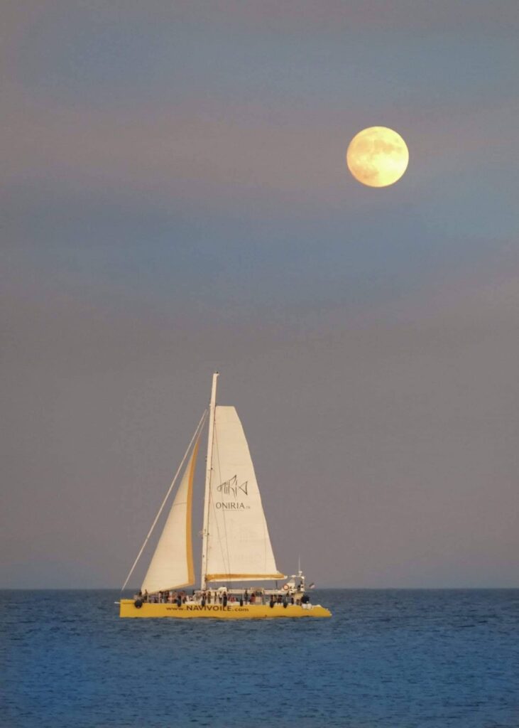 Coucher de soleil à Canet-en-Roussillon : le catamaran Navivoile sous voiles au crépuscule avec un lever de lune en arrière-plan