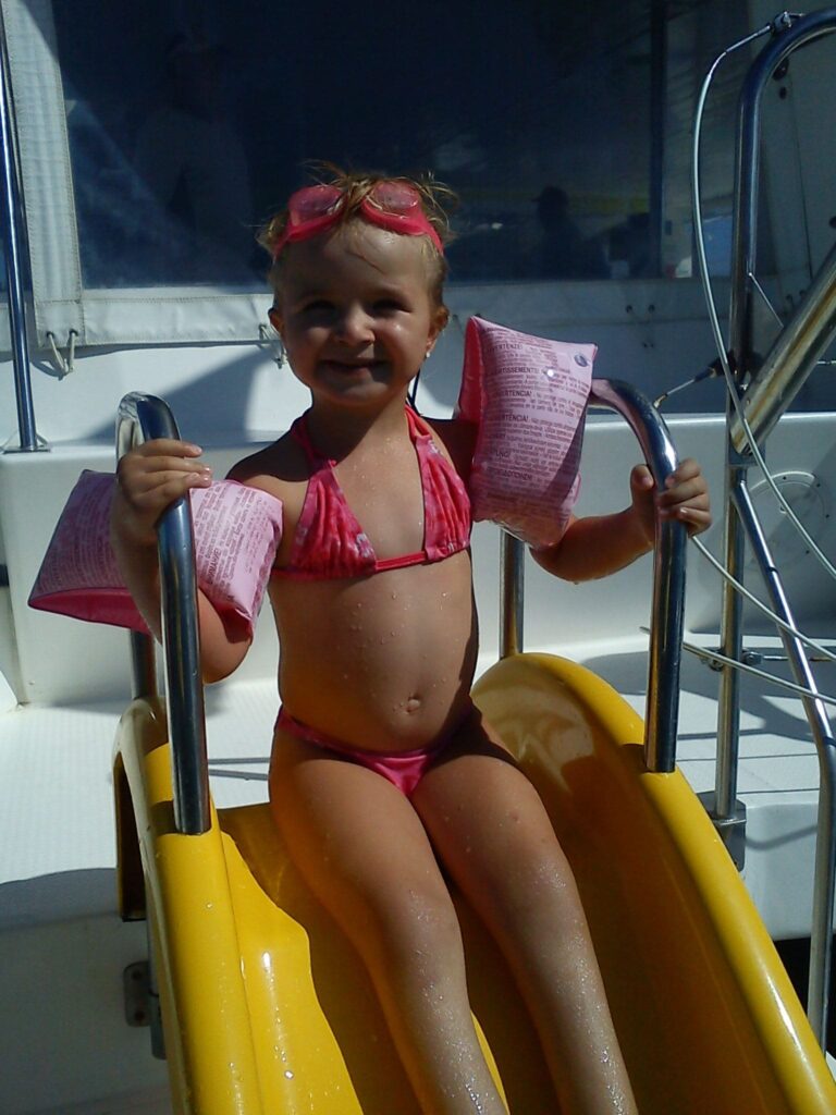 Une petite fille portant des brassards de sécurité colorés, prête à se lancer sur le toboggan arrière du catamaran dans les eaux cristallines de Paulilles lors d'une Sortie bateau Canet
