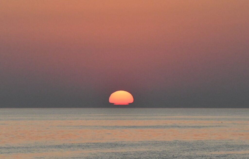 Photographie panoramique d'une Sortie en Mer au Lever du Soleil. Le disque solaire s'élève au-dessus des flots comme un mirage, créant une illusion d'optique sur l'horizon méditerranéen lors d'une session d'observation de dauphin à bord du catamaran Navivoile