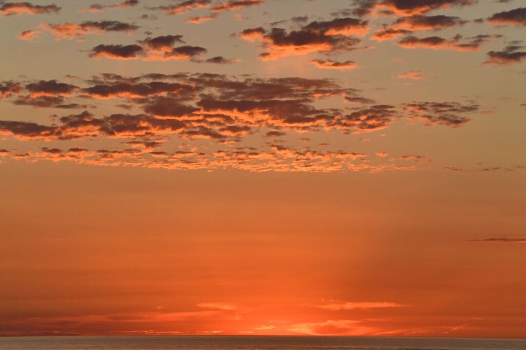 Photo d'une Sortie en Mer au Lever du Soleil au large d'Argelès-sur-Mer. L'horizon s'illumine juste avant que le soleil ne perce la surface, par une belle matinée d'été calme, lors d'une excursion d'observation de dauphin à bord du catamaran Navivoile