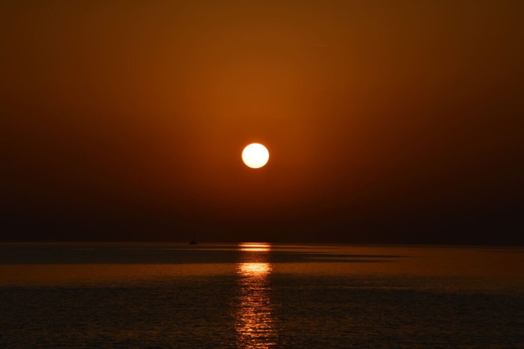 Photo d'une Sortie en Mer au Lever du Soleil face à l'étang marin de Canet-Saint-Nazaire. Le ciel est d'un doré intense au-dessus d'une mer sombre et plate, lors d'une excursion d'observation de dauphin à bord du catamaran Navivoile