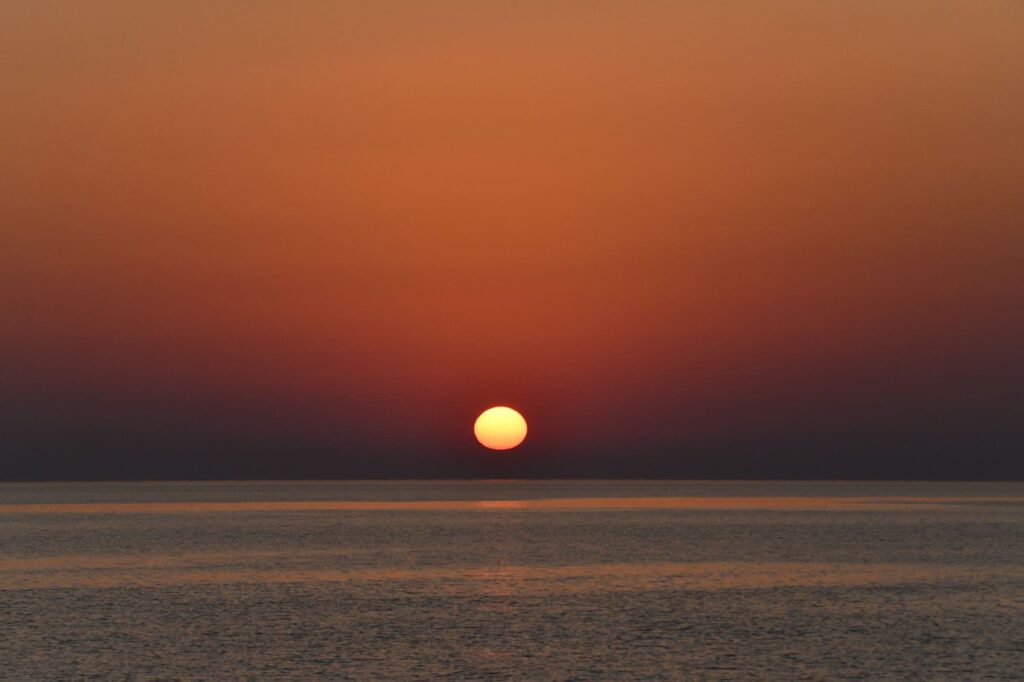Photo d'une Sortie en Mer au Lever du Soleil au large de Barcarès. Le disque solaire vient de percer l'horizon depuis quelques minutes, embrasant le ciel de couleurs chaudes lors d'une session d'observation de dauphin à bord du catamaran Navivoile