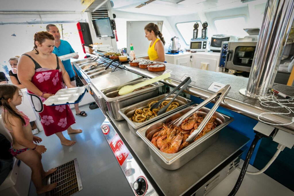 Une famille se servant au buffet du catamaran Navivoile, choisissant des gambas, calamars et saucisses catalanes grillés lors d'une escapade culinaire en mer au départ de Canet