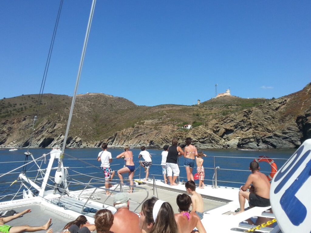 Le catamaran Navivoile naviguant à l'entrée de l'anse Sainte-Catherine derrière le Cap Béar, avec le sémaphore de la Marine Nationale dominant la falaise lors d'une Sortie en mer à Canet-en-Roussillon