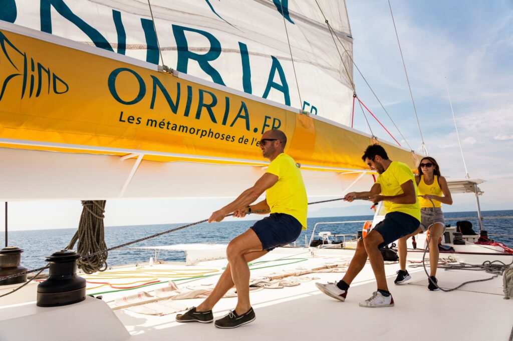 L'équipage du catamaran Navivoile hissant la grand-voile Oniria à la force des bras juste devant l'entrée du port de Canet-en-Roussillon