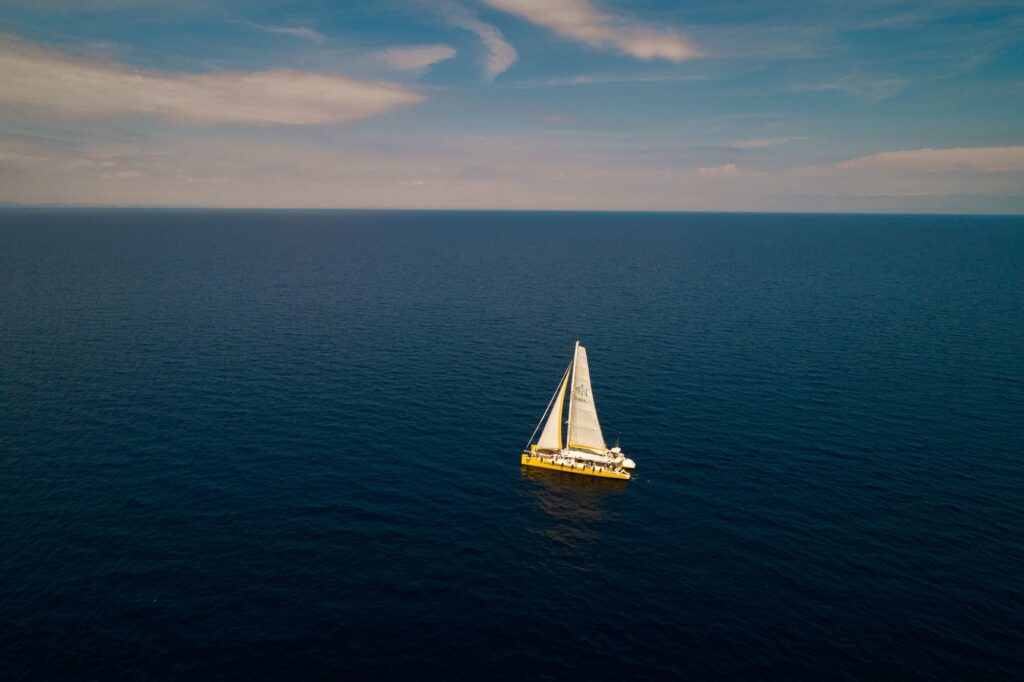 Vue aérienne de très loin du catamaran Navivoile sous voiles au milieu de l'immensité bleue de la Méditerranée