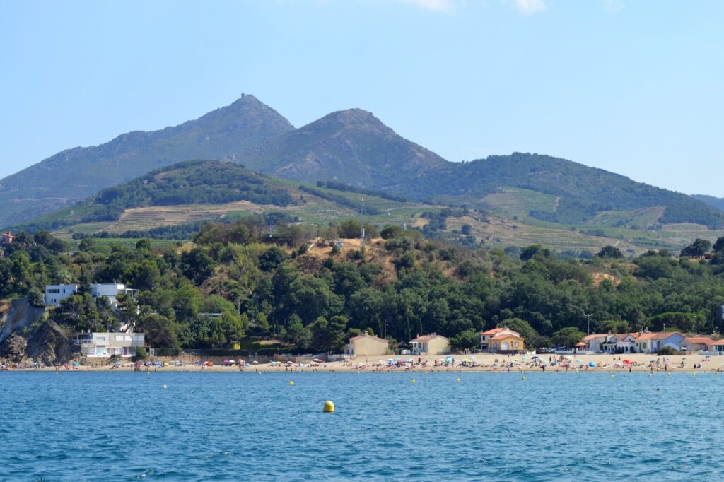 Le catamaran Navivoile naviguant devant la plage du Racou à Argelès-sur-Mer, avec la Tour de la Massane du XIIIe siècle dominant la colline en arrière-plan lors d'une Sortie en mer à Canet-en-Roussillon