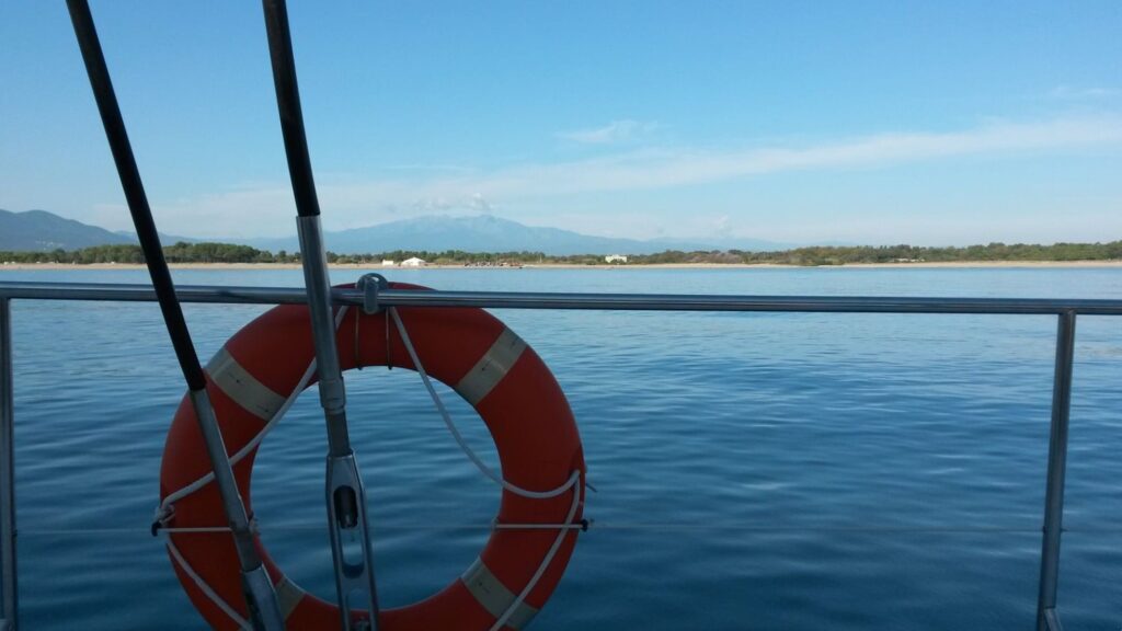 Le catamaran Navivoile naviguant le long de la plage entre Saint-Cyprien et Argelès-sur-Mer avec le sommet enneigé du Massif du Canigou en arrière-plan lors d'une Sortie en mer à Canet-en-Roussillon