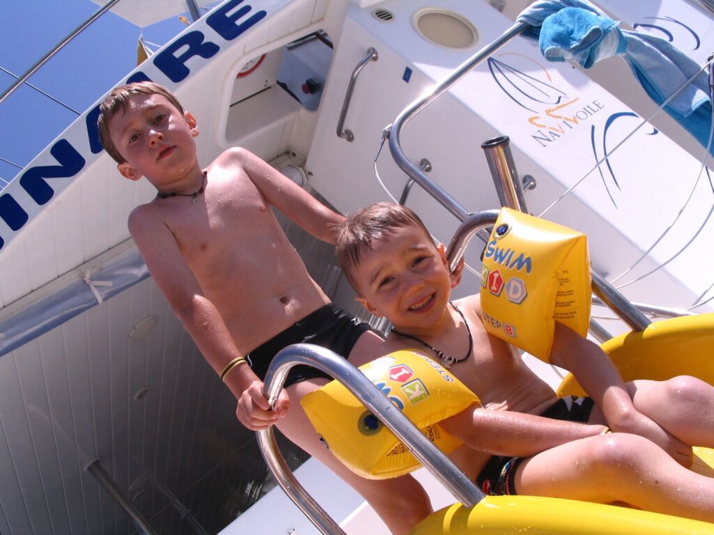 Deux enfants prêts à glisser sur le toboggan du catamaran Navivoile pour plonger dans les eaux chaudes et translucides de la baie de Paulilles, lors d'une expédition maritime au départ de Canet