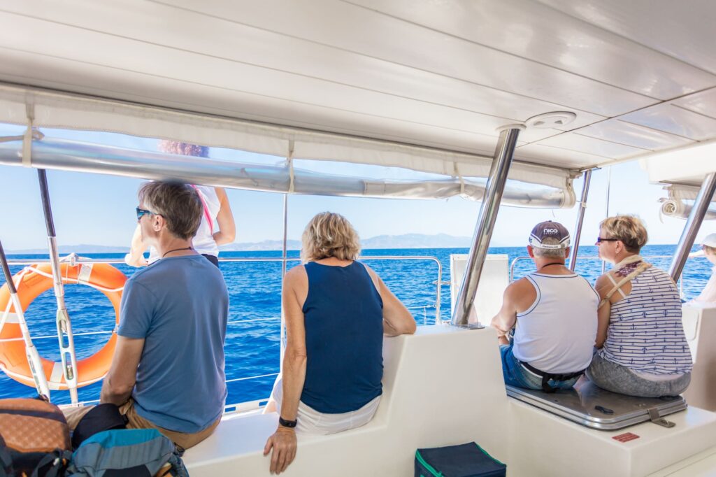 Vue de dos de passagers en contemplation face à la mer Méditerranée et à la côte rocheuse escarpée au loin, lors d'une matinée d'été calme pour une observation dauphins Port-Vendres avec le catamaran Navivoile