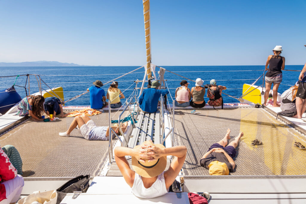 Passagers du catamaran Navivoile assis et allongés sur les filets avant, contemplant l'horizon par temps calme lors d'une Sortie en mer à Canet-en-Roussillon