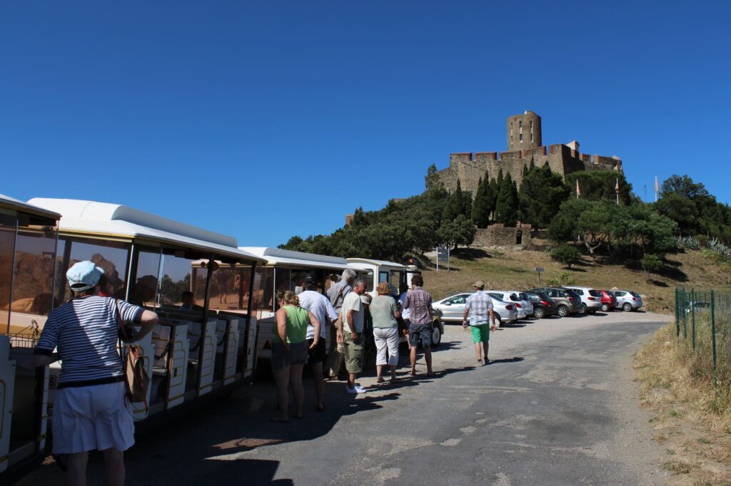 Le petit train touristique à l'arrêt devant l'imposant Fort Saint-Elme surplombant la baie de Collioure et Port-Vendres