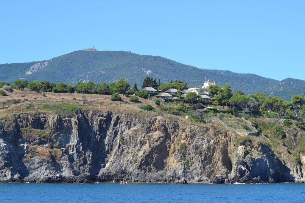 Photo en navigation sous voiles lors d'une Promenade en mer à Port-Vendres. Le catamaran Navivoile longe les criques sauvages de Porteils, avec la tour de la Massane dominant le sommet des Albères en arrière-plan