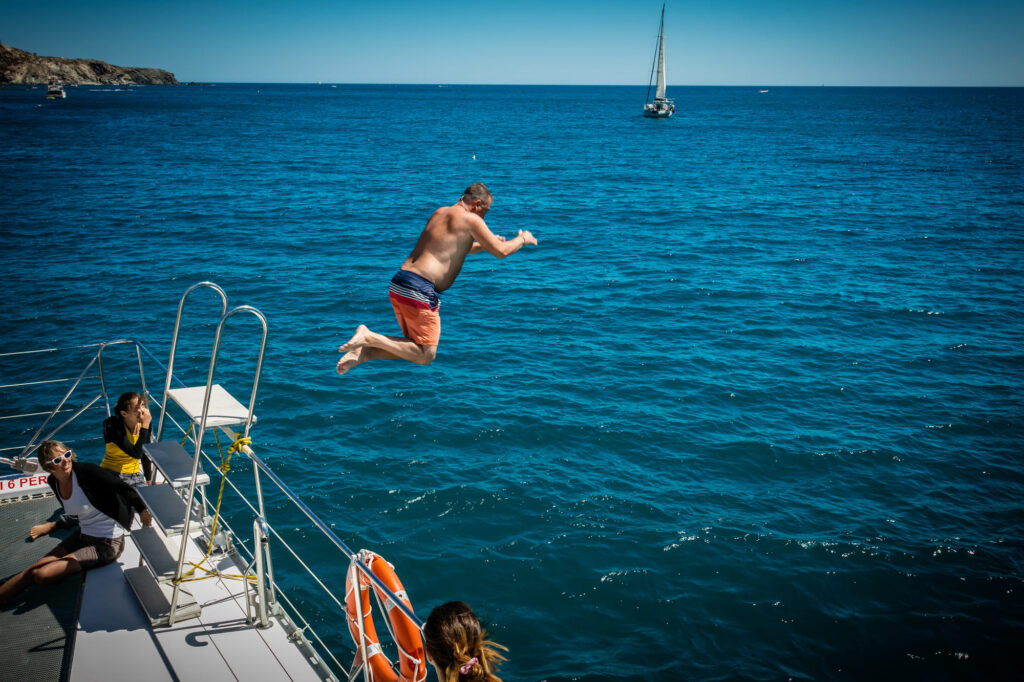 Passager sautant verticalement depuis le plongeoir du navire de la compagnie Navivoile dans les eaux claires de l'anse de Paulilles, durant une escapade marine avec escale gourmande au départ de Canet-en-Roussillon