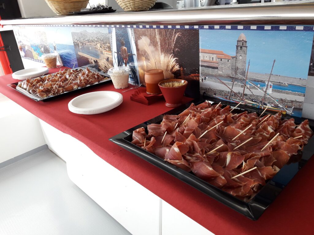 Présentation d'un buffet de charcuterie catalane dans la nacelle du NAVIVOILE lors d'une activité pour groupe devant le clocher de Collioure