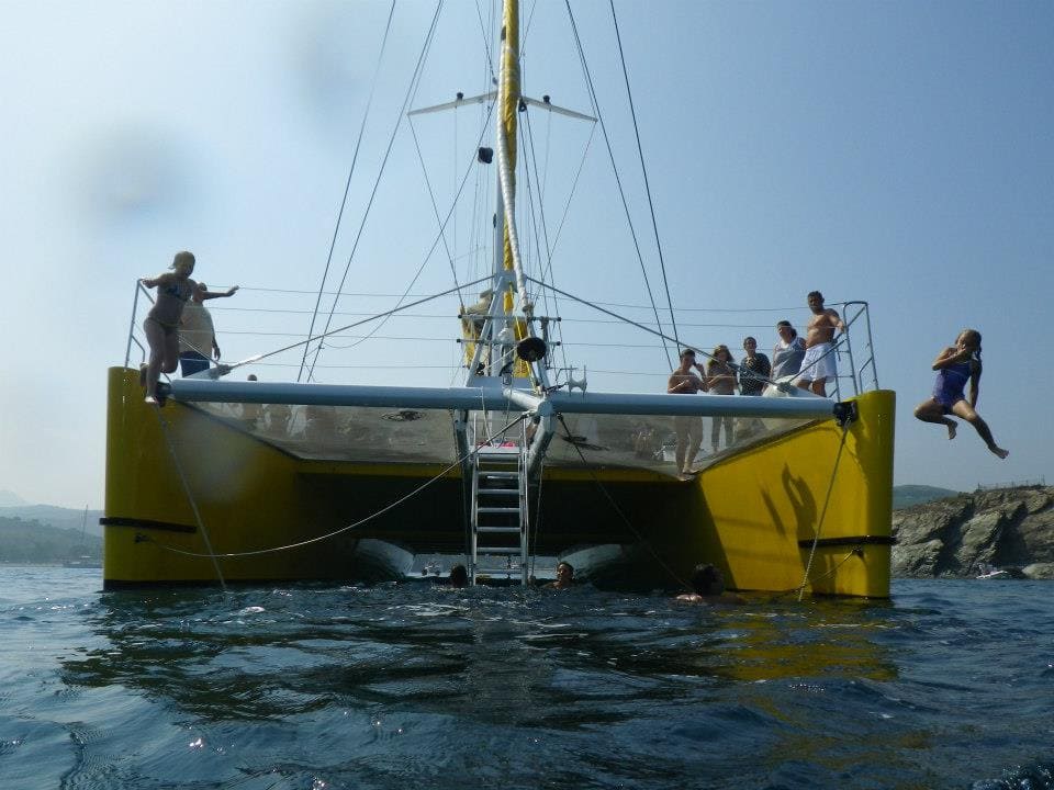 Un enfant saute dans l'eau turquoise depuis l'avant du catamaran Navivoile dans la Baie de Paulilles. Scène de joie lors d'une croisière Grillades et Baignade avec le principal catamaran à voile à Canet-en-Roussillon et Port-Vendres