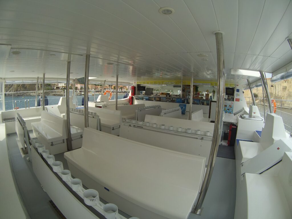 Vue intérieure au Fish Eye de l'arrière de la nacelle du catamaran Navivoile avec ses tables et tablettes. Navire à quai à Canet-en-Roussillon, à proximité immédiate de l'aquarium Oniria