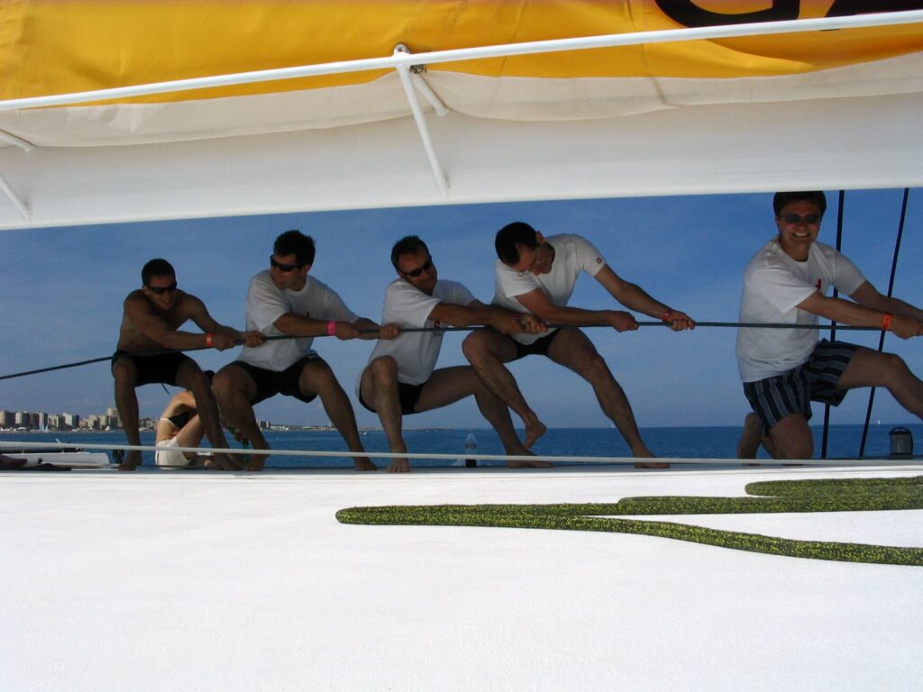 Groupe d'amis en EVG participant à la manœuvre pour hisser la grand-voile du NAVIVOILE au départ du port de Canet-en-Roussillon lors d'une activité pour groupe