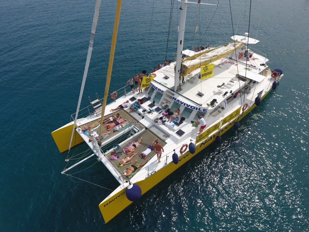 Vue aérienne par drone d'un groupe en voyage incentive, se baignant et se relaxant sur les filets avant du NAVIVOILE au mouillage dans la baie de Paulilles