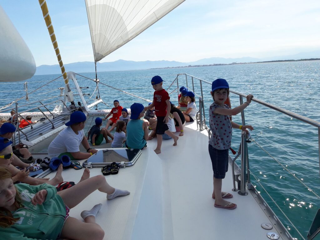 Des enfants de primaire installés sur le pont tribord et dans les filets du Navivoile en navigation silencieuse à la voile devant l'Étang de Canet-Saint-Nazaire