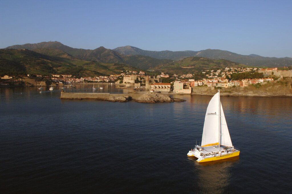 Navigation contemplative au large de Collioure : vue panoramique sur le massif des Albères et la cité des peintres depuis le pont du catamaran NAVIVOILE lors d'un voyage en groupé organisé à bord du catamaran